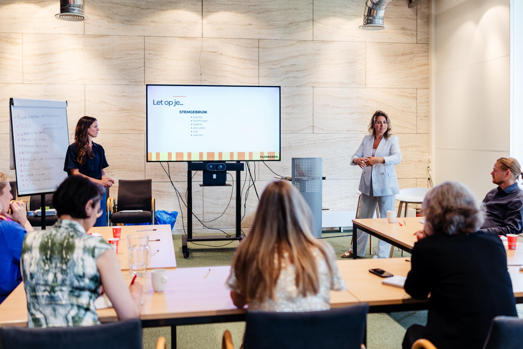 Sarah geeft een presentatie voor een scherm terwijl deelnemers meekijken